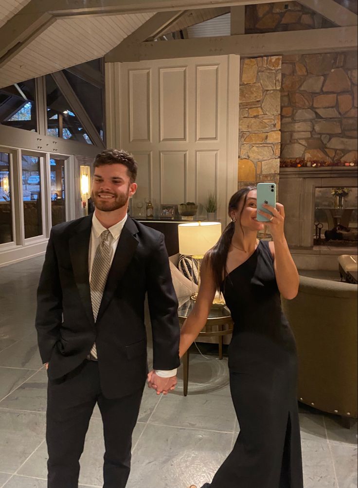 a man and woman in formal wear walking through a living room holding each other's hands