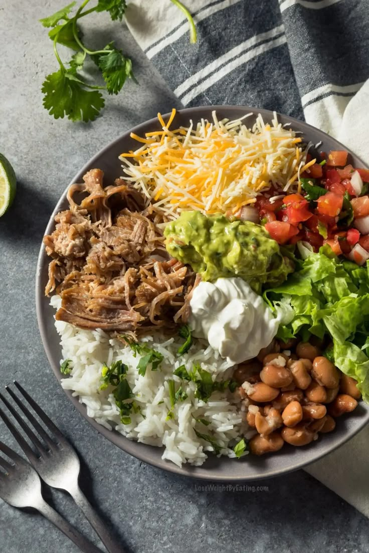 a bowl filled with rice, beans, meat and guacamole on top of a table