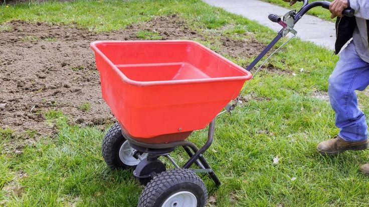 a man pushing a red wheelbarrow in the grass