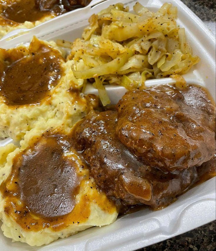 a white plate topped with mashed potatoes and meat covered in gravy next to other food