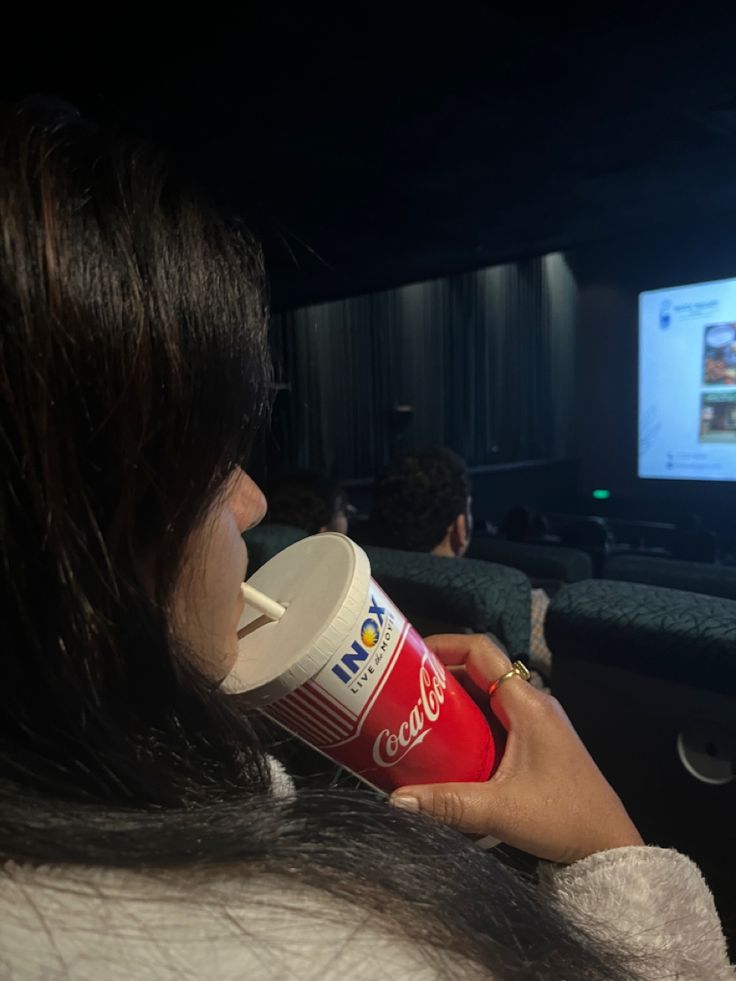 a woman drinking from a cup in front of a screen