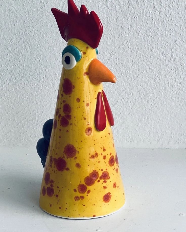 a yellow and red rooster figurine sitting on top of a white table next to a wall