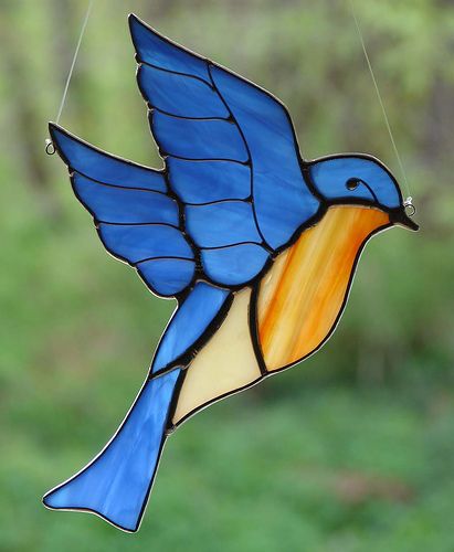 a stained glass bird hanging from a string in front of a green grass covered field