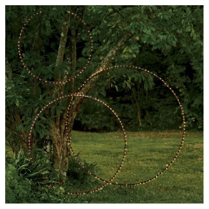 an outdoor sculpture made out of string lights in the middle of a field with trees and grass