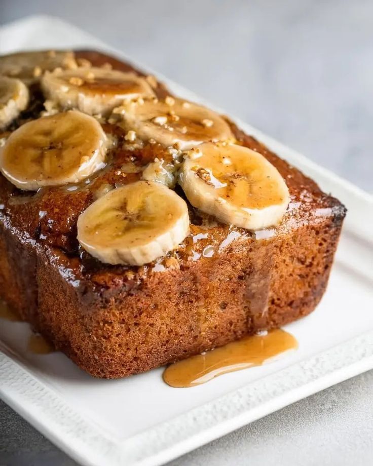 a piece of banana bread on a white plate with caramel sauce drizzled around it