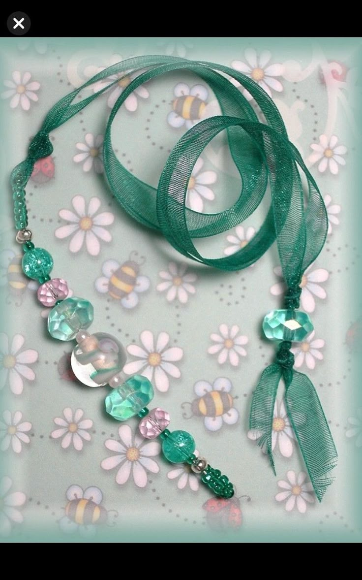 a green necklace with flowers and beads on it's side, next to a flowery background