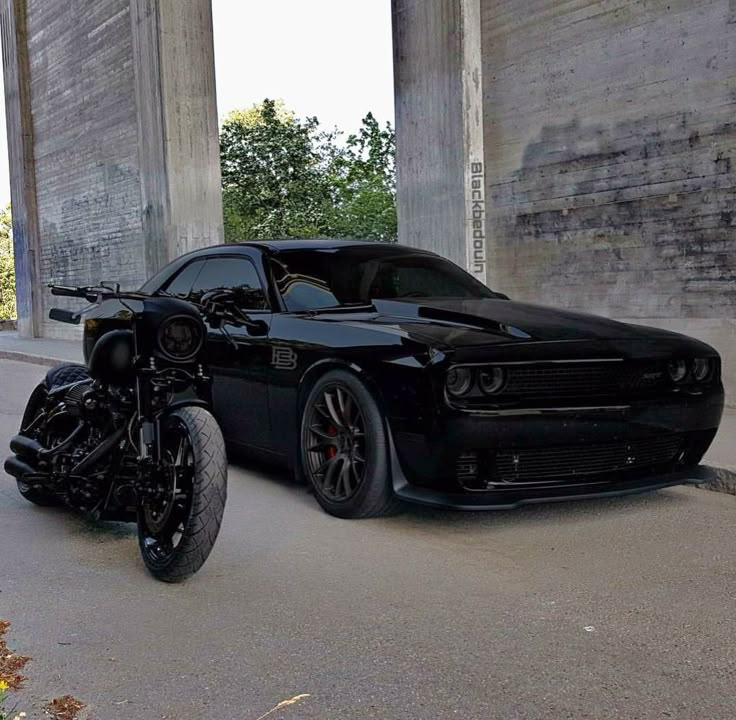 a black car parked next to a motorcycle on the street in front of an overpass