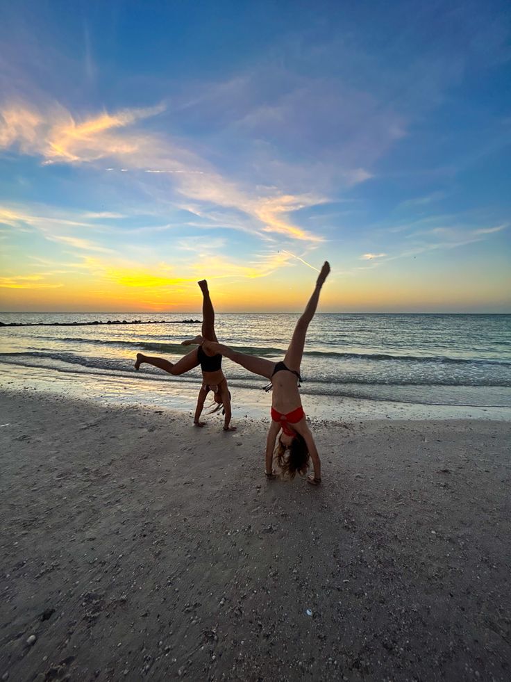 two people doing handstands on the beach at sunset