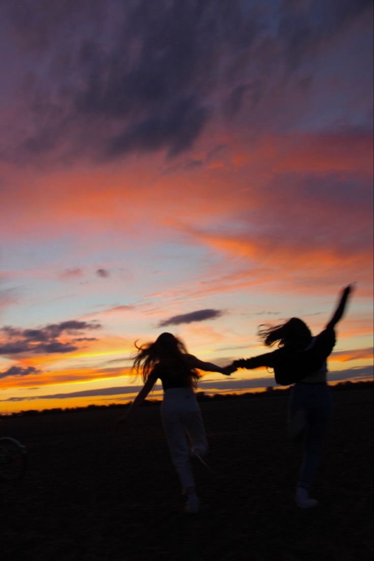 two women are playing with a frisbee at sunset