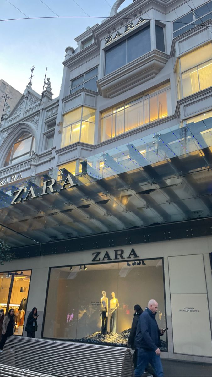 people are walking in front of a store with glass windows and an awning over the entrance