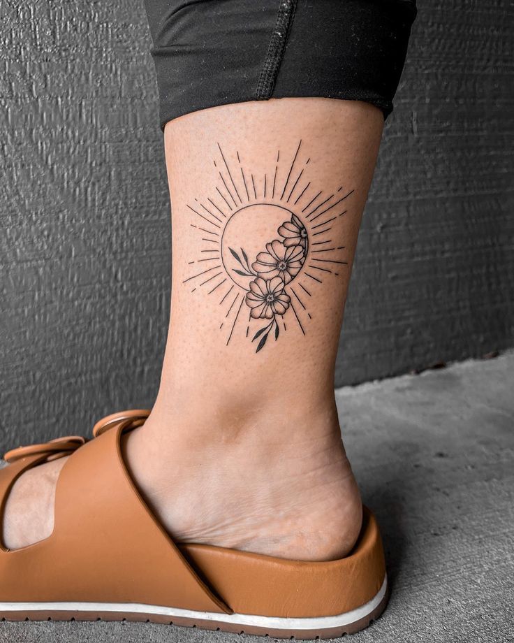 a woman's foot with a sun and flowers tattoo on the side of her leg