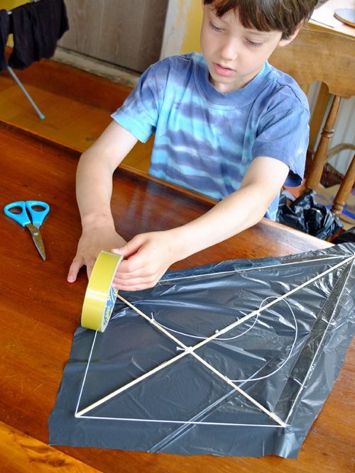 a young boy is making a kite out of duct tape and some scissors on the table