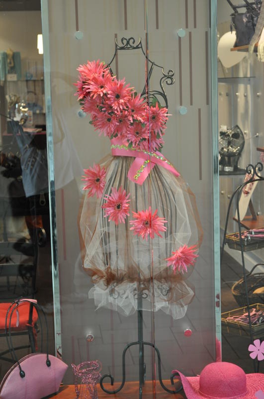 a pink hat is on display in a store window with flowers and other items behind it