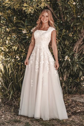 a woman standing in front of trees wearing a wedding dress