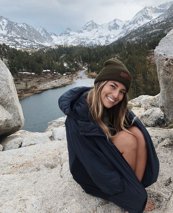 a woman sitting on top of a large rock next to a lake in the mountains