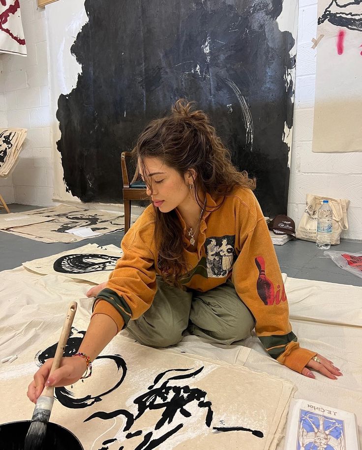 a woman is sitting on the floor working on some art work with brush and ink