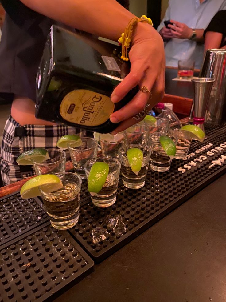 the bartender is pouring shots into glasses with limes