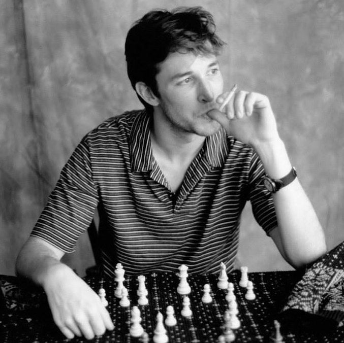 a man sitting at a table with a chess board and pieces in front of him