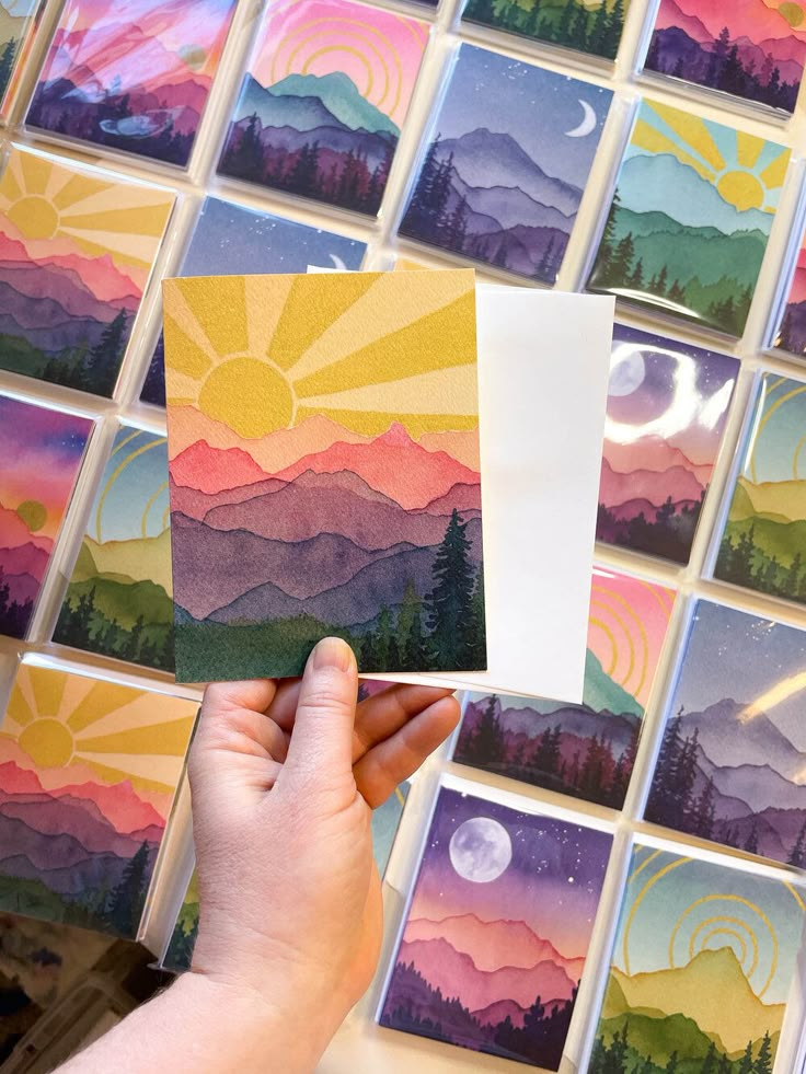 someone is holding up some cards with mountains and trees on them in front of a mosaic wall