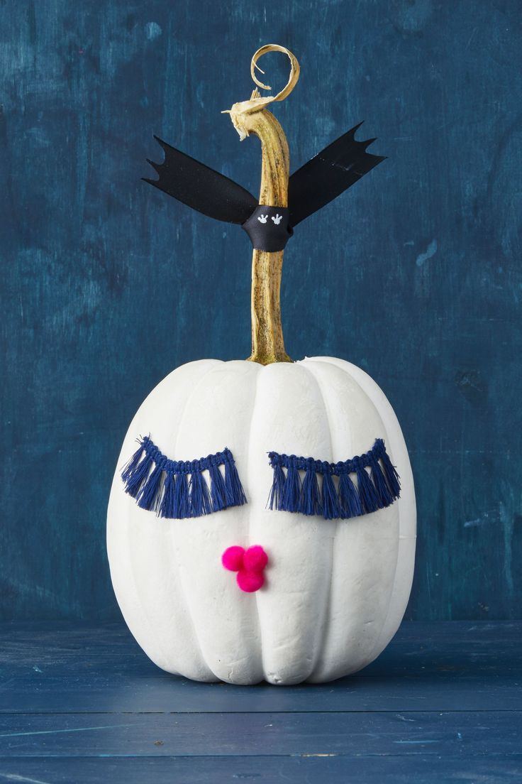 a white pumpkin with blue fringes and eyes painted gold on it's face