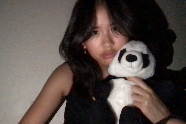 a woman holding a white and black stuffed panda bear in her right hand while wearing a black top