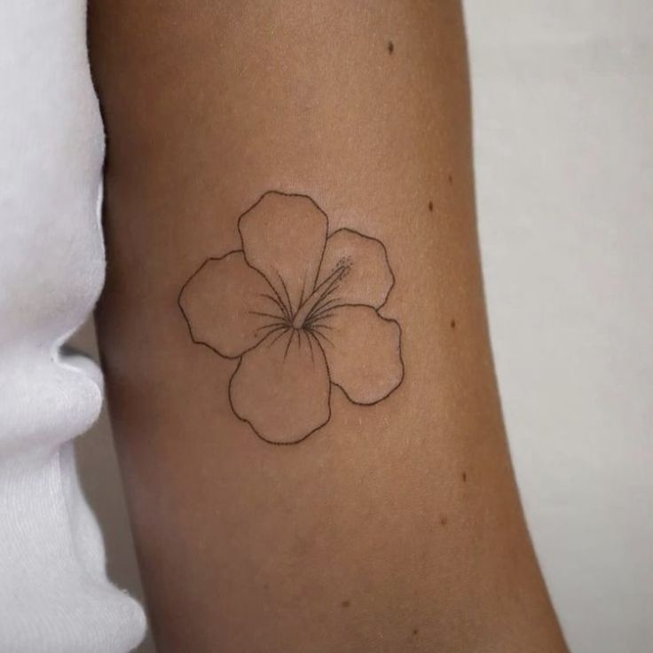 a small flower tattoo on the left side of the arm is shown in black ink