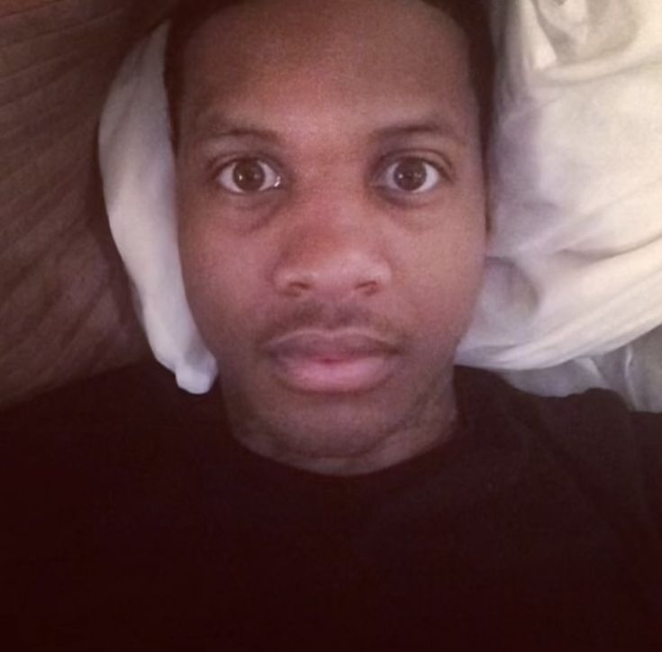 a man laying in bed with white sheets on his head and looking at the camera