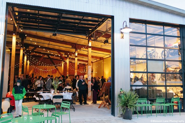 people are walking into an open building with green tables and chairs