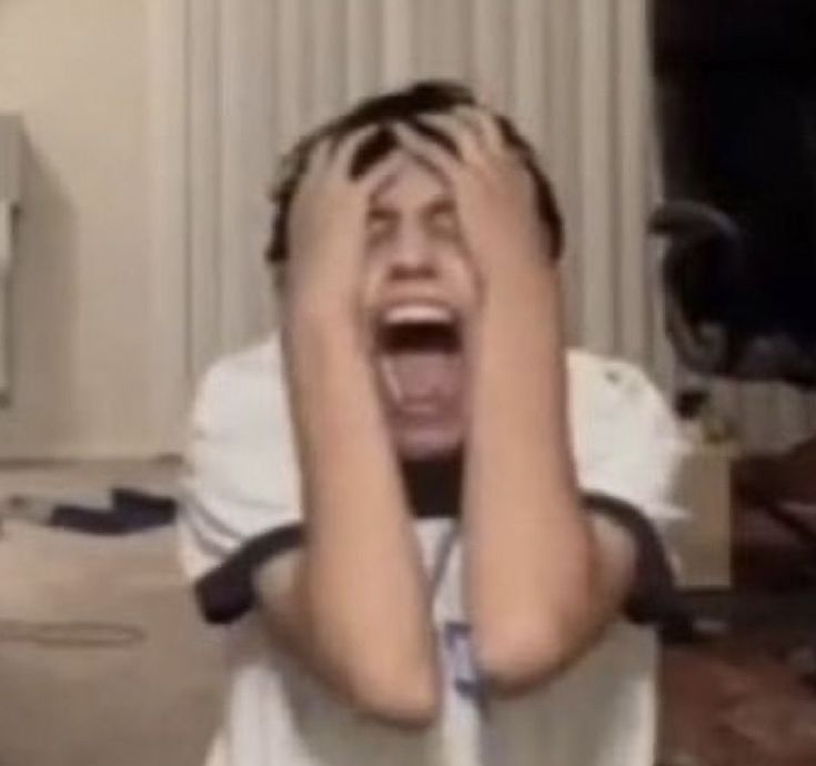 a young boy holding his hands up to his face while screaming in the living room