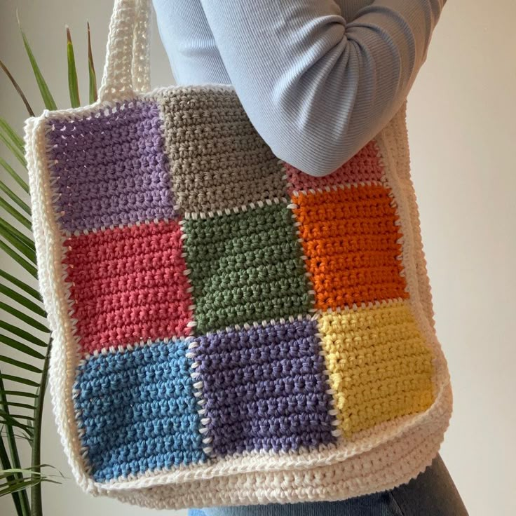 a woman is holding a multicolored crocheted tote bag in her hands