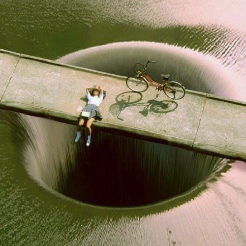 a man laying on top of a large hole in the water next to a bike