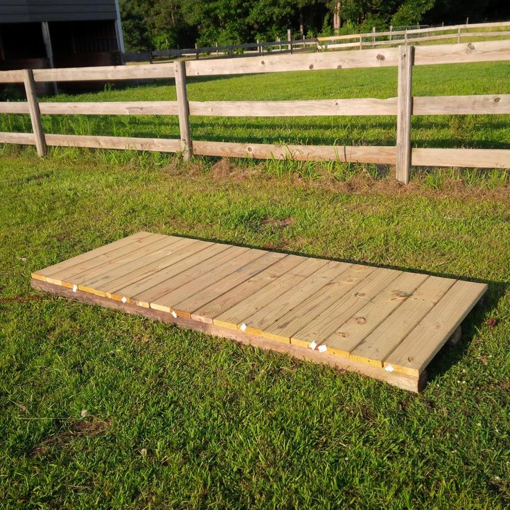 a wooden platform sitting in the middle of a field next to a fence and grass