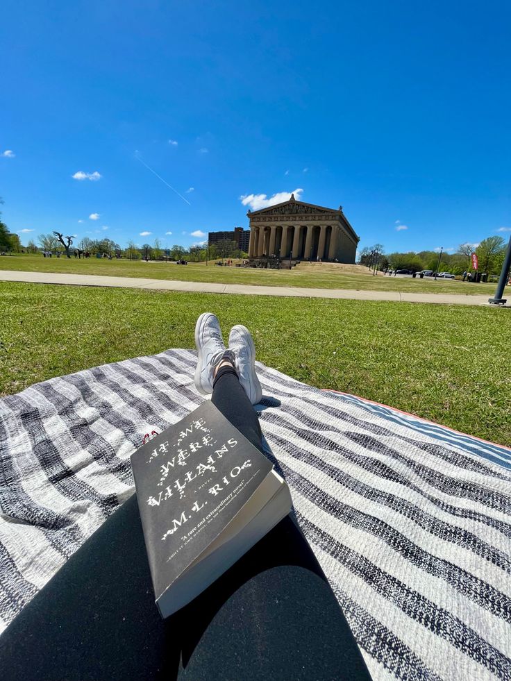 a person sitting on top of a blanket with a book in front of them and a building behind them