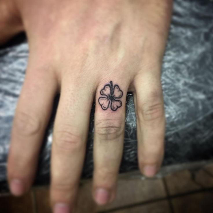 a person's hand with a small clover tattoo on the middle finger and an inked four leaf clover