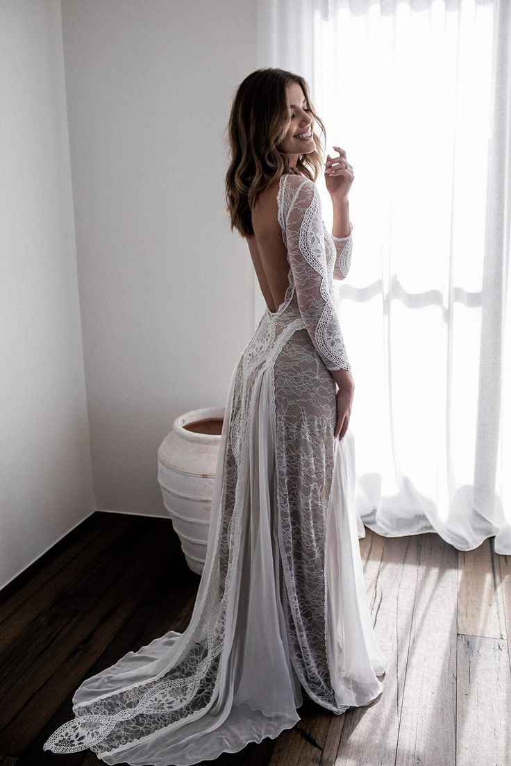 a woman standing in front of a window with her back to the camera and wearing a white dress