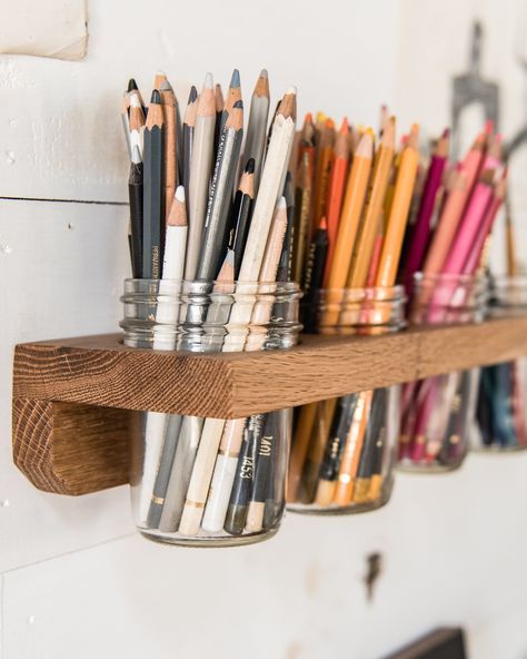 several pencils are lined up in mason jars on a wooden shelf next to a white wall