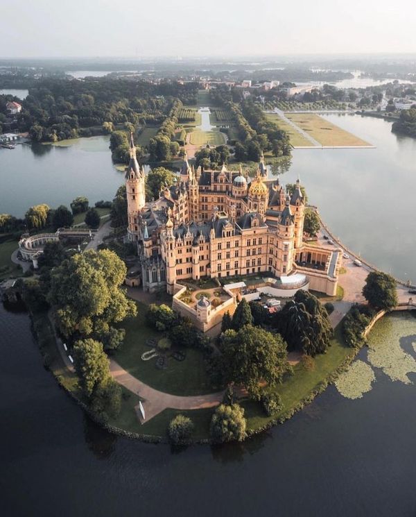 an aerial view of a castle in the middle of a lake with trees around it