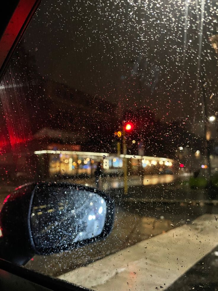 rain is falling on the windshield of a car in front of a red traffic light