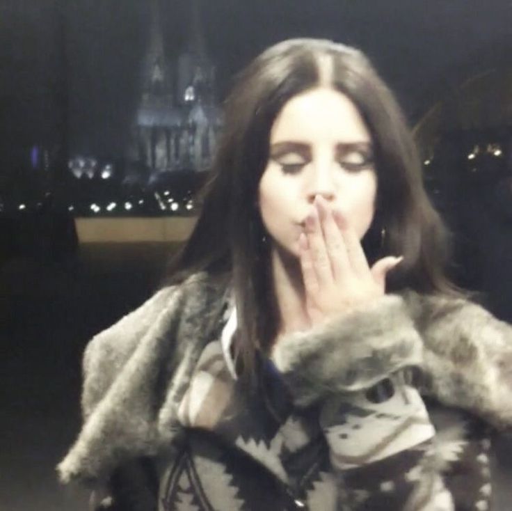 a woman in a fur coat is making a hand gesture with her mouth while standing outside at night