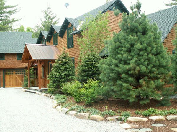 a large house with lots of trees in the front yard and gravel driveway leading up to it