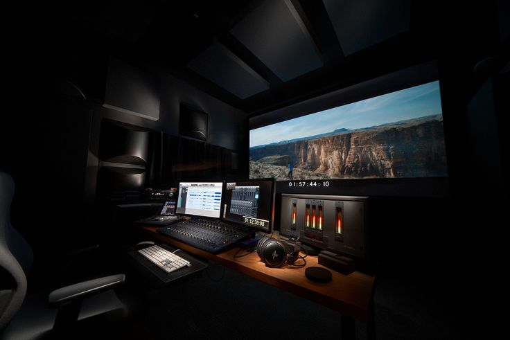 a computer desk topped with two monitors and a keyboard in front of a large screen