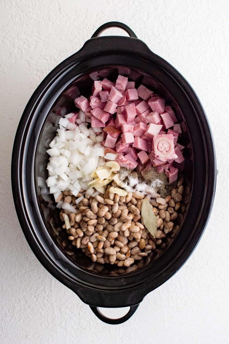 an overhead view of food in a crock pot with onions, ham and beans