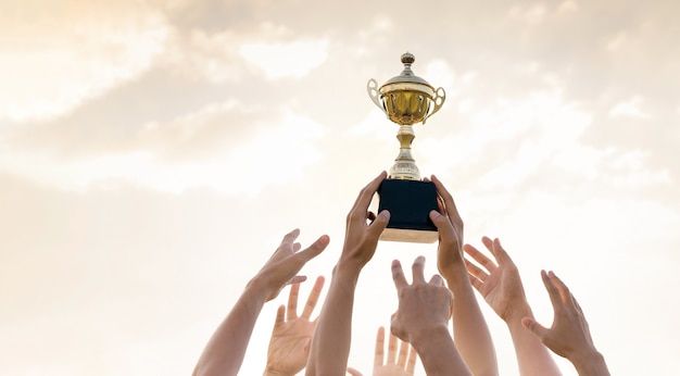 many hands are reaching up toward a trophy in the air with it's base on top