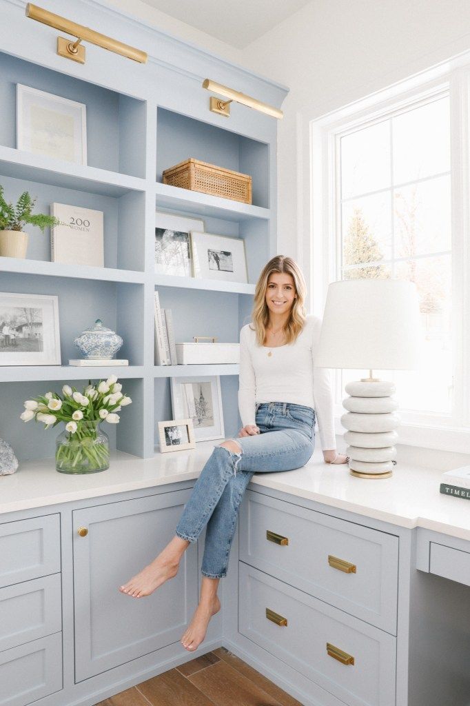 a woman sitting on top of a white counter next to a shelf filled with books