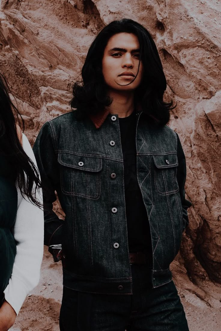 two people standing next to each other in front of a rock wall and wearing denim jackets