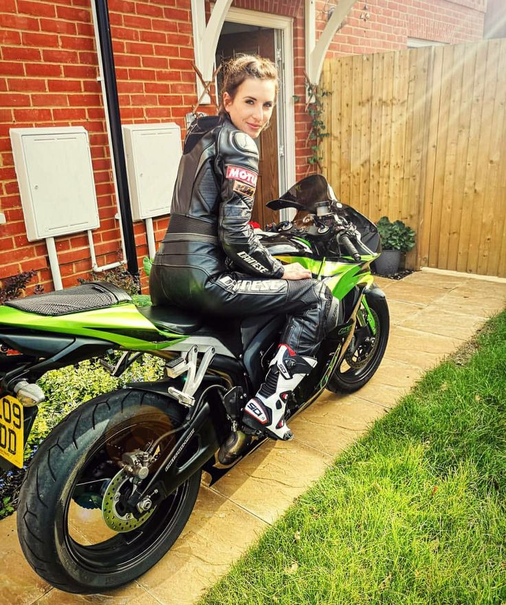 a woman sitting on top of a motorcycle in front of a brick building and green grass