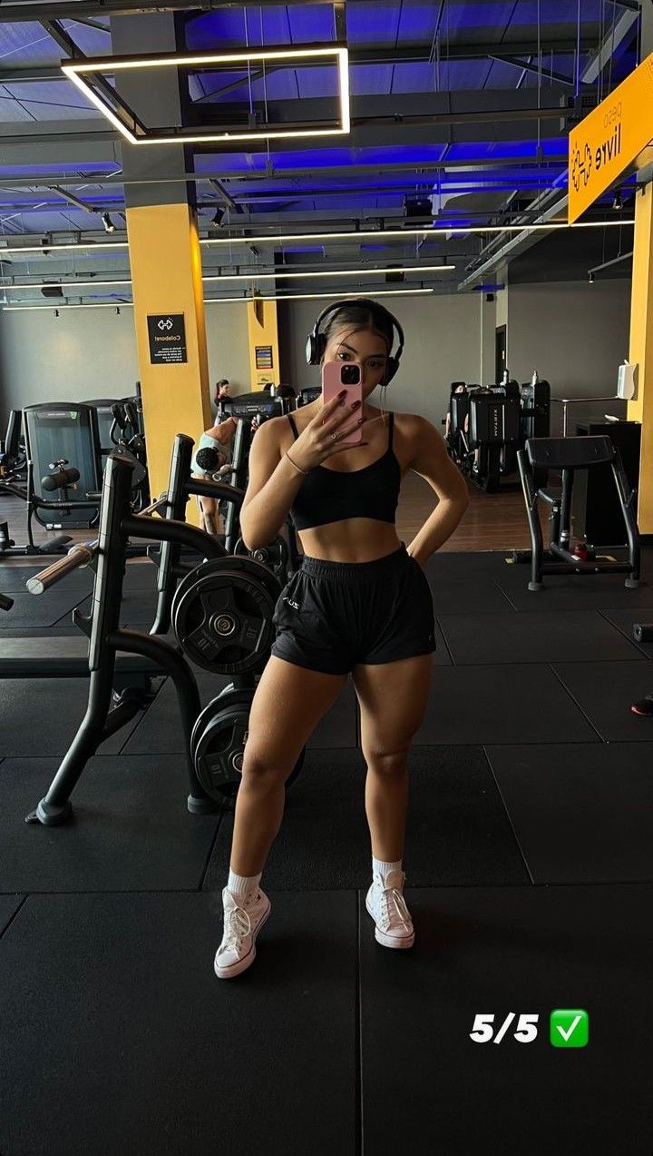 a woman is taking a selfie in the gym with headphones on and looking at her phone