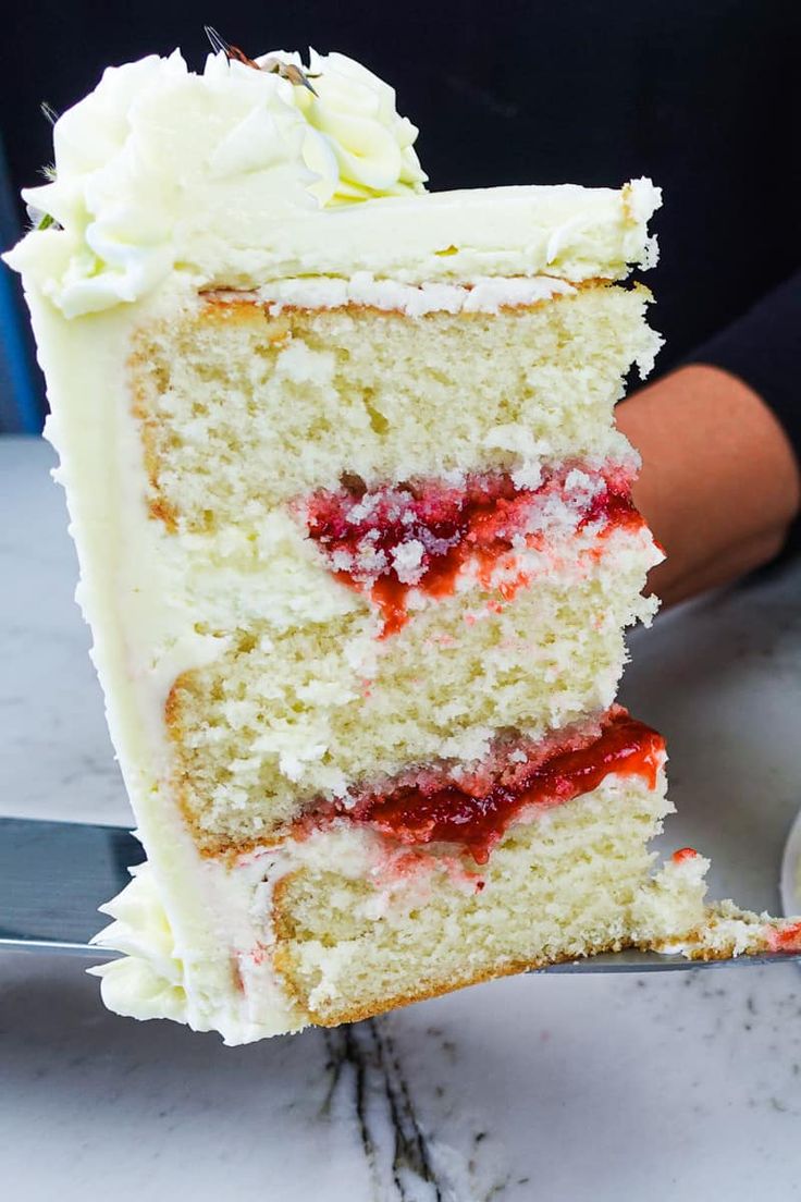 a slice of cake with white frosting and strawberries is being held by a person