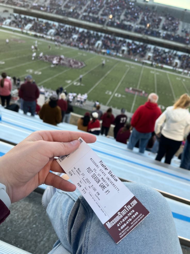 a person holding a ticket in their hand at a football game with people watching from the bleachers