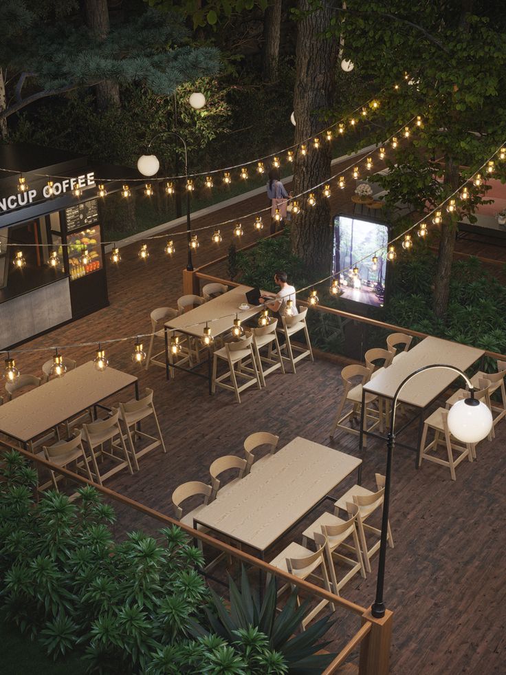 an outdoor seating area with tables and chairs, lights strung from the trees around it